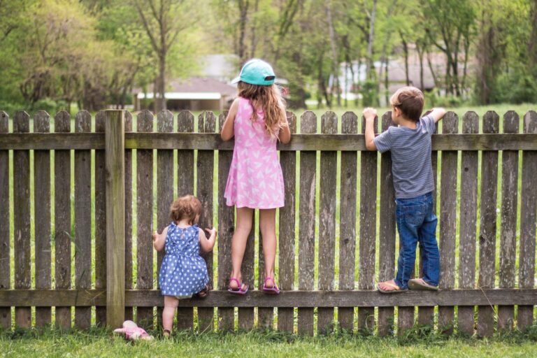 Curious children looking over a fence while playing together in a backyard.